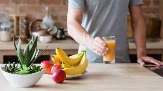 Мужчина выпивает стакан воды рядом с контейнером с разными фруктами.