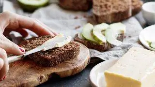 Изображение женской руки, наносящей масло на тост.