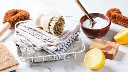 Куча чистящих тряпок с щеткой рядом с совой с пищевой содой и разрезанным лимоном.