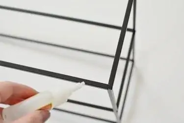 Ручное нанесение клея Gorilla на черную металлическую раму стеллажа на белом фоне