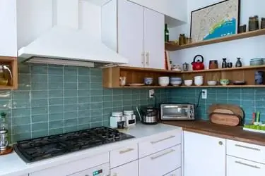 кухня с фартуком из синей плитки, белыми шкафчиками, белой вытяжкой и плитой