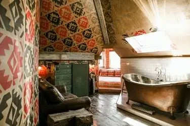 ванная комната с состаренным деревянным полом, потертым кожаным диваном и металлической ванной на ножках под потолочным окном ванная комната с состаренным деревянным полом, потертым кожаным диваном и металлической ванной на ножках под потолочным окном