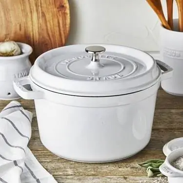 Белая голландская печь Staub на столешнице с другими кухонными предметами